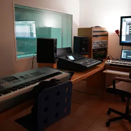 A quiet home production room with a keyboard, monitors and screens, nobody at the desk.