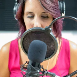 Someone recording into a studio microphone wearing headphones.